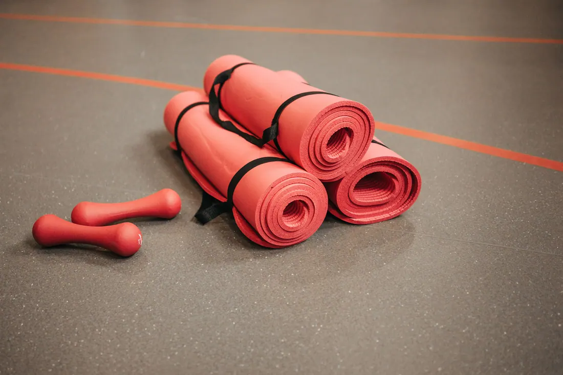 Esterillas enrolladas y pesas sobre el suelo de un gimnasio