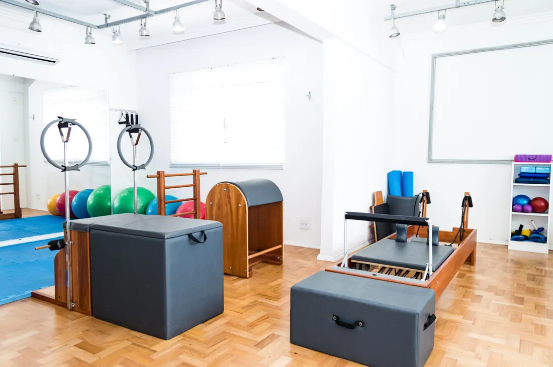 Sala de ejercicio vacía con suelo de madera, esterillas enrolladas y luz natural suave