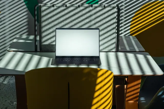 Portátil con pantalla en blanco sobre una mesa con luces de persiana