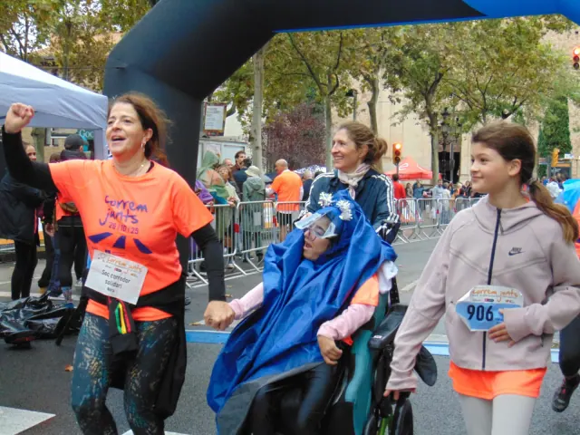 Un grupo de participantes cruza el arco de meta de la carrera solidaria "Correm Junts