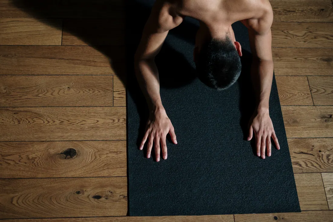 Un hombre practica yoga sobre una esterilla en un suelo de madera