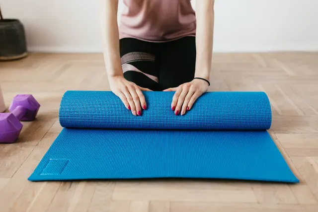 Una mujer enrolla una esterilla de yoga azul en el suelo