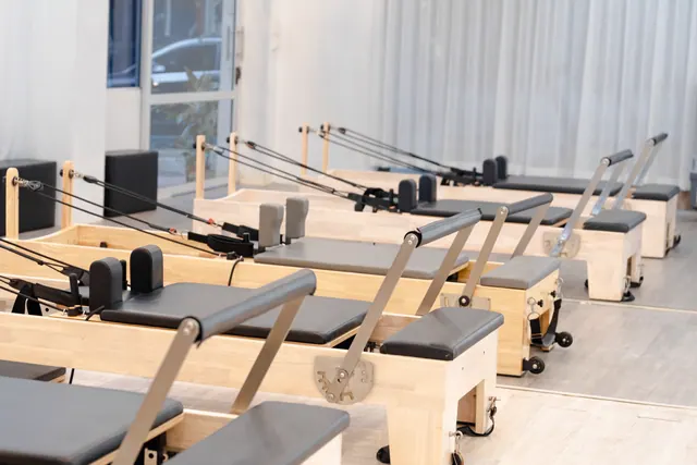 Estudio de pilates vacío con una máquina reformer de madera, una colchoneta enrollada y luz natural