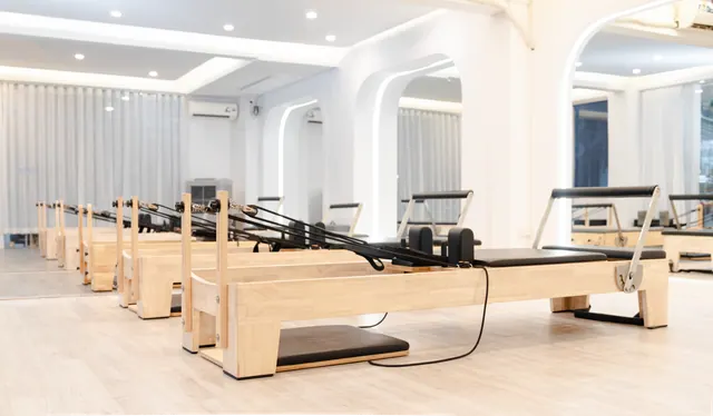 Estudio de pilates con reformer de madera, silla con pedal y barril curvo, sin personas