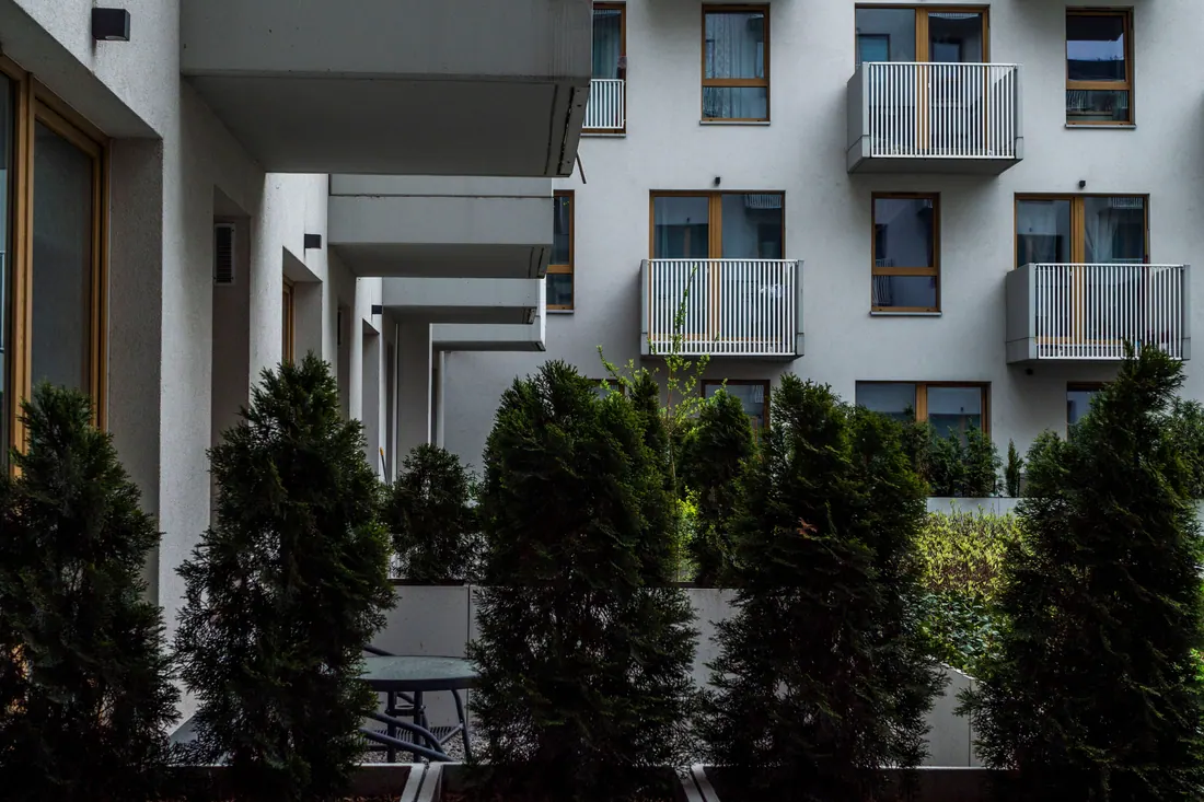 Fachada de edificio residencial moderno con balcones, ventanas de madera y setos verdes en primer plano