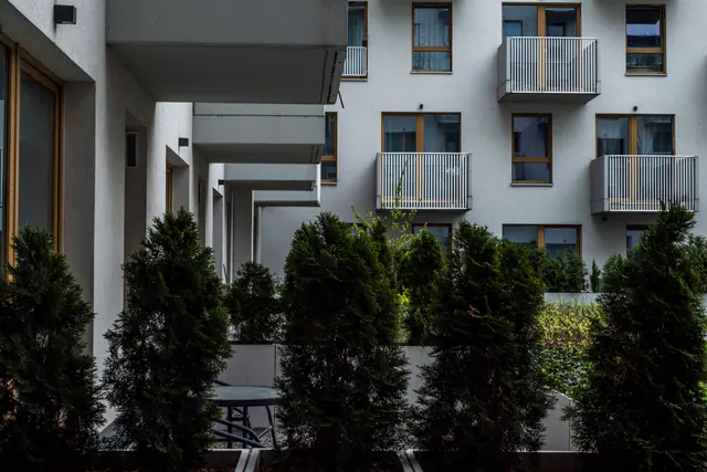 Fachada de edificio residencial moderno con balcones, ventanas de madera y setos verdes en primer plano