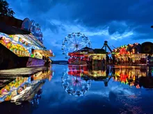 Una feria nocturna con noria iluminada y atracciones reflejadas en el suelo mojado