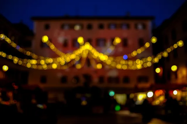 Plaza nocturna decorada con guirnaldas amarillas de luces, fachada de edificio histórico al fondo