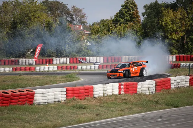 Vehículo deportivo naranja derrapando en circuito delimitado por neumáticos pintados en rojo y blanco, generando humo