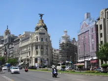 Amplia avenida urbana con edificios señoriales a ambos lados, tráfico y peatones circulando por las aceras