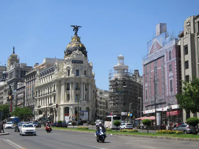 Amplia avenida urbana con edificios señoriales a ambos lados, tráfico y peatones circulando por las aceras