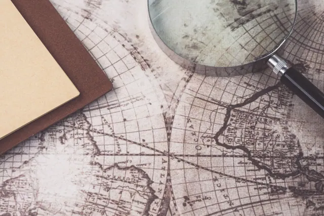 Lupa y cuaderno sobre mapas antiguos y documentos de cartografía sobre una superficie de madera