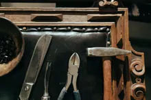 Herramientas de tapicería como martillo y tenazas apoyadas sobre un mueble de madera tallada con tachuelas