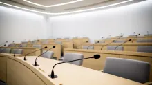 Aula de conferencias con filas de pupitres de madera clara y asientos grises, equipadas con micrófonos negros