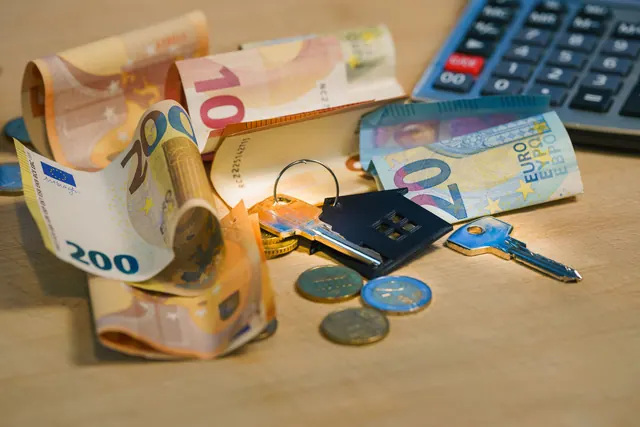 Billetes de euro, monedas y llaves con llavero en forma de casa