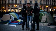 Agentes de policía controlan a una persona en una plaza pública con acampadas