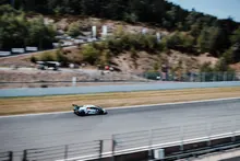 Un coche de carreras a gran velocidad en un circuito rodeado de colinas