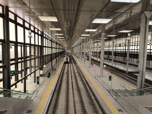 Andenes de una estación de tren con varios convoyes detenidos junto a las vías y paneles informativos
