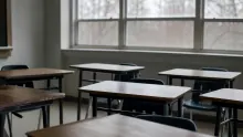 Aula vacía con varios pupitres de madera y metal distribuidos ante una ventana con vistas a árboles desnudos
