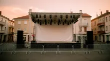 Escenario al aire libre con estructura metálica, pantalla blanca y focos, montado en una plaza con vallas