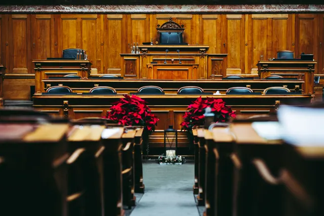 Interior de una sala de sesiones o tribunal con mobiliario de madera noble, sillas de cuero negro y flores