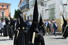Procesión religiosa avanzando por una calle engalanada entre vecinos que observan el ambiente festivo