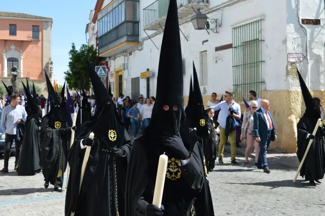 Procesión religiosa avanzando por una calle engalanada entre vecinos que observan el ambiente festivo