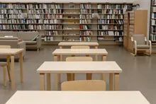 Interior de biblioteca con estanterías repletas de libros y mesas de madera con sillas en primer plano