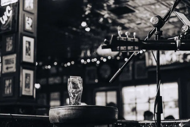 Un vaso de cristal sobre un taburete junto a una guitarra y un micrófono en un bar en penumbra