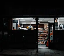 Fachada de un pequeño comercio cerrado con escaparates iluminados y estanterías con productos en el interior