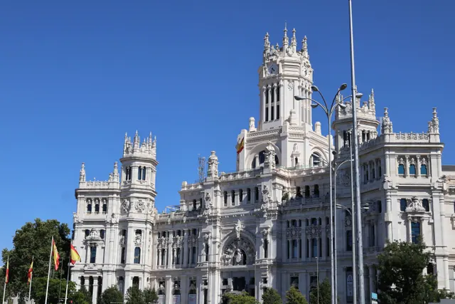 Fachada de un imponente edificio histórico de piedra clara con torres, ventanales y detalles ornamentales