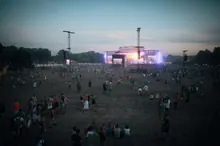 Público de espaldas asistiendo a un concierto al aire libre, con las manos en alto frente al escenario iluminado