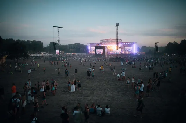 Público de espaldas asistiendo a un concierto al aire libre, con las manos en alto frente al escenario iluminado