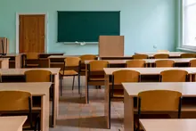 Aula escolar vacía con pupitres de madera, sillas individuales y pizarra verde en la pared