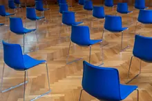 Sillas azules con estructura metálica distribuidas sobre un suelo de parqué en un espacio interior vacío