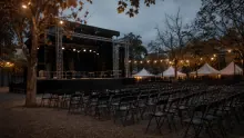 Escenario de concierto montado en un parque nocturno con carpas blancas de fondo