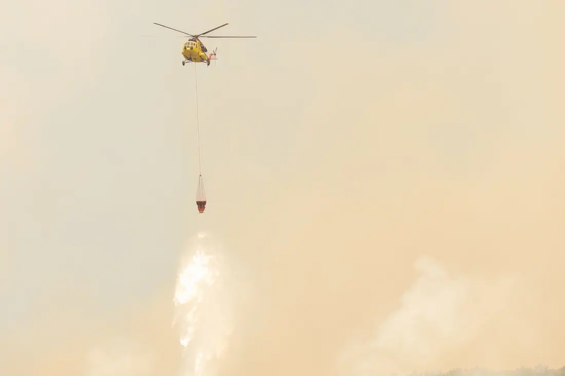 Helicóptero de extinción de incendios descargando agua sobre una zona con humo