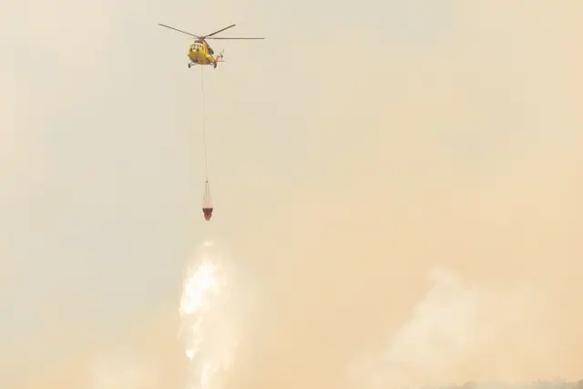 Helicóptero de extinción de incendios descargando agua sobre una zona con humo