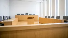 Sala de vistas con mobiliario de madera clara, tribunal elevado al fondo y sillas grises dispuestas en los laterales