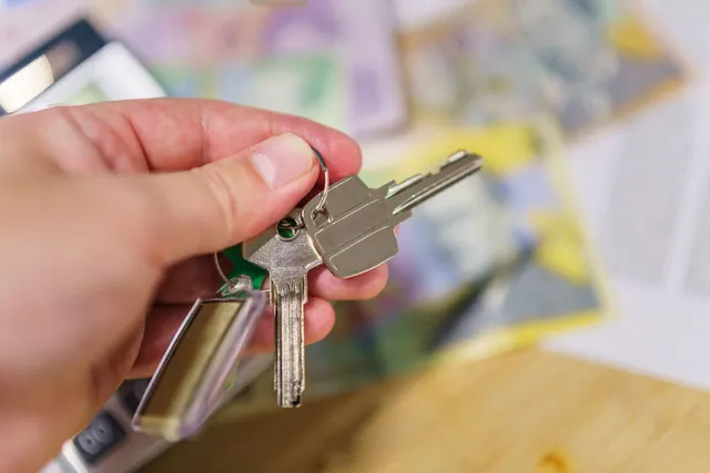 Una mano sostiene unas llaves sobre una mesa con documentos de fondo