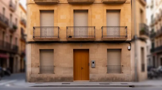 Fachada de edificio de dos plantas de color ocre con puerta central de madera oscura, ventanas y balcones