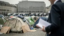 Campamento de tiendas en plaza urbana con vehículos policiales de fondo