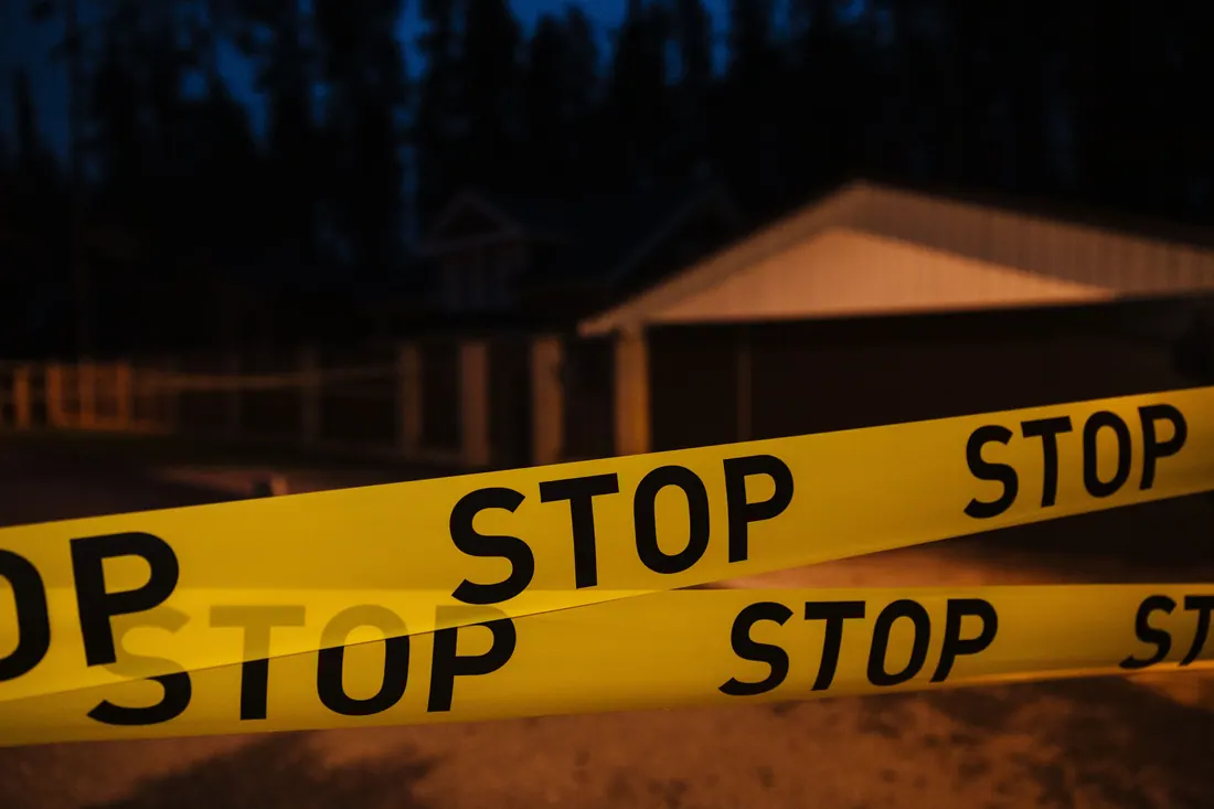 Cinta policial amarilla con la palabra STOP frente a una vivienda de noche