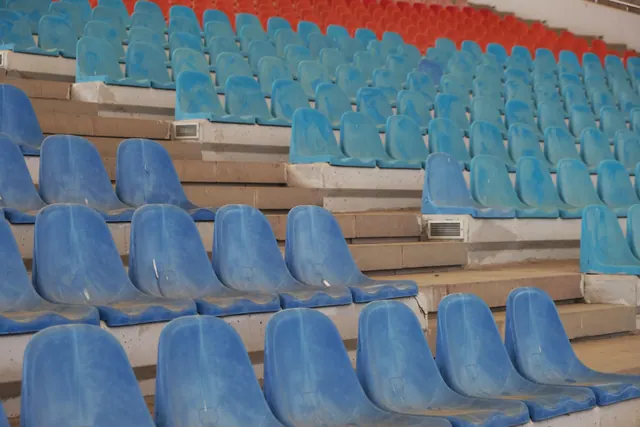 Gradas vacías de un estadio con asientos azules y rojos