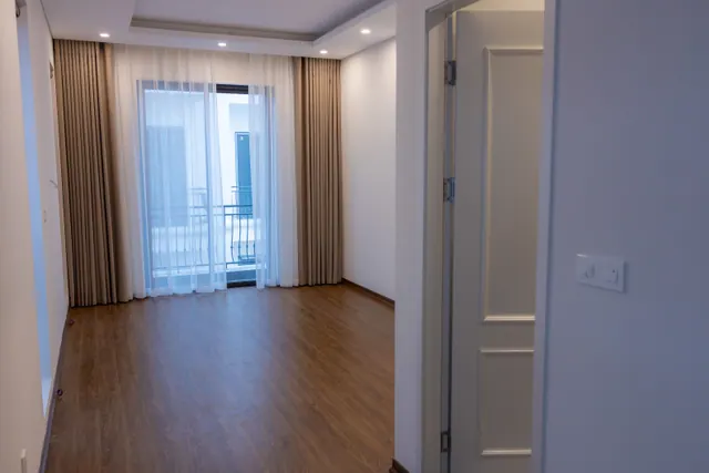 Interior de apartamento moderno vacío con suelo de madera, cortinas beige y balcón con vistas a la ciudad