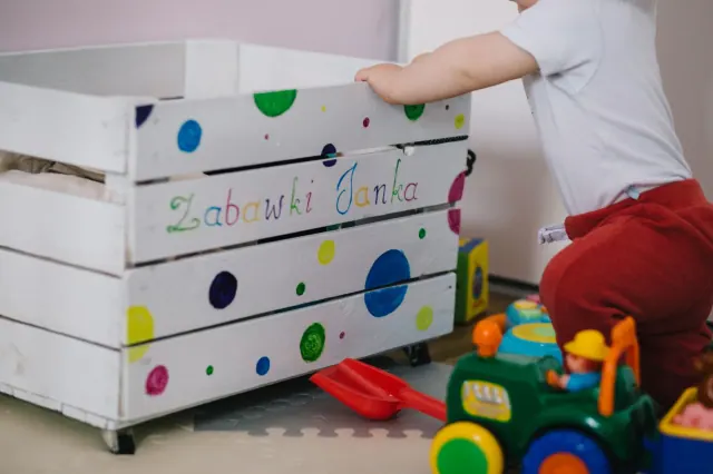 Un niño se apoya en un baúl de madera decorado con lunares de colores