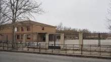 Edificio de ladrillo con pórtico de columnas y cercado metálico en zona despoblada