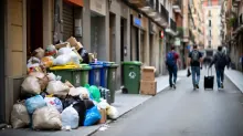 Dos contenedores de basura junto a un muro y una señal