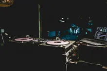 Equipo de DJ con tornamesas, mezclador y portátil sobre una mesa en ambiente oscuro de discoteca