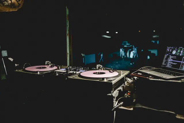 Equipo de DJ con tornamesas, mezclador y portátil sobre una mesa en ambiente oscuro de discoteca